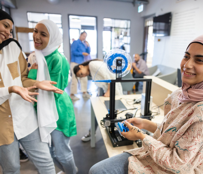 Three girls laughing while working with a 3D printer.