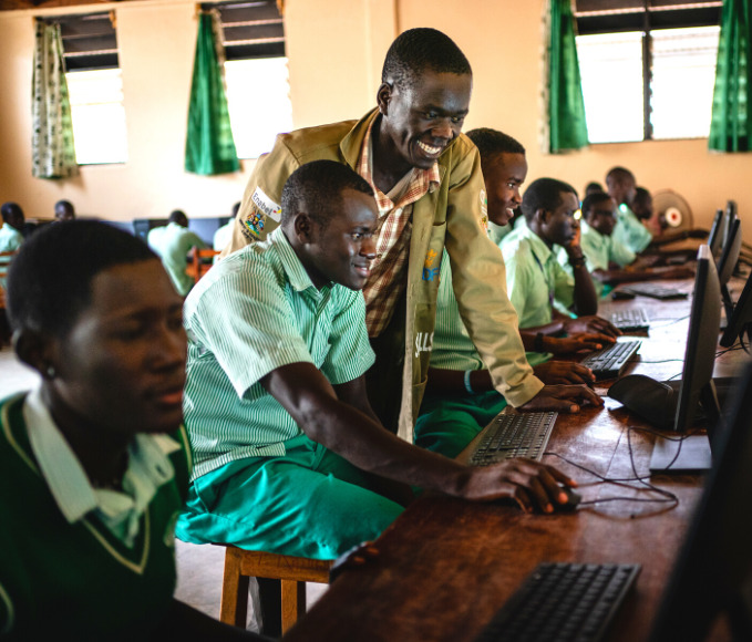 A teacher showing a student in Uganda how to search for something on a computer in the computer lab of the school.