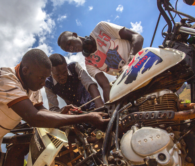 Three young men working on a motorcycle in Uganda