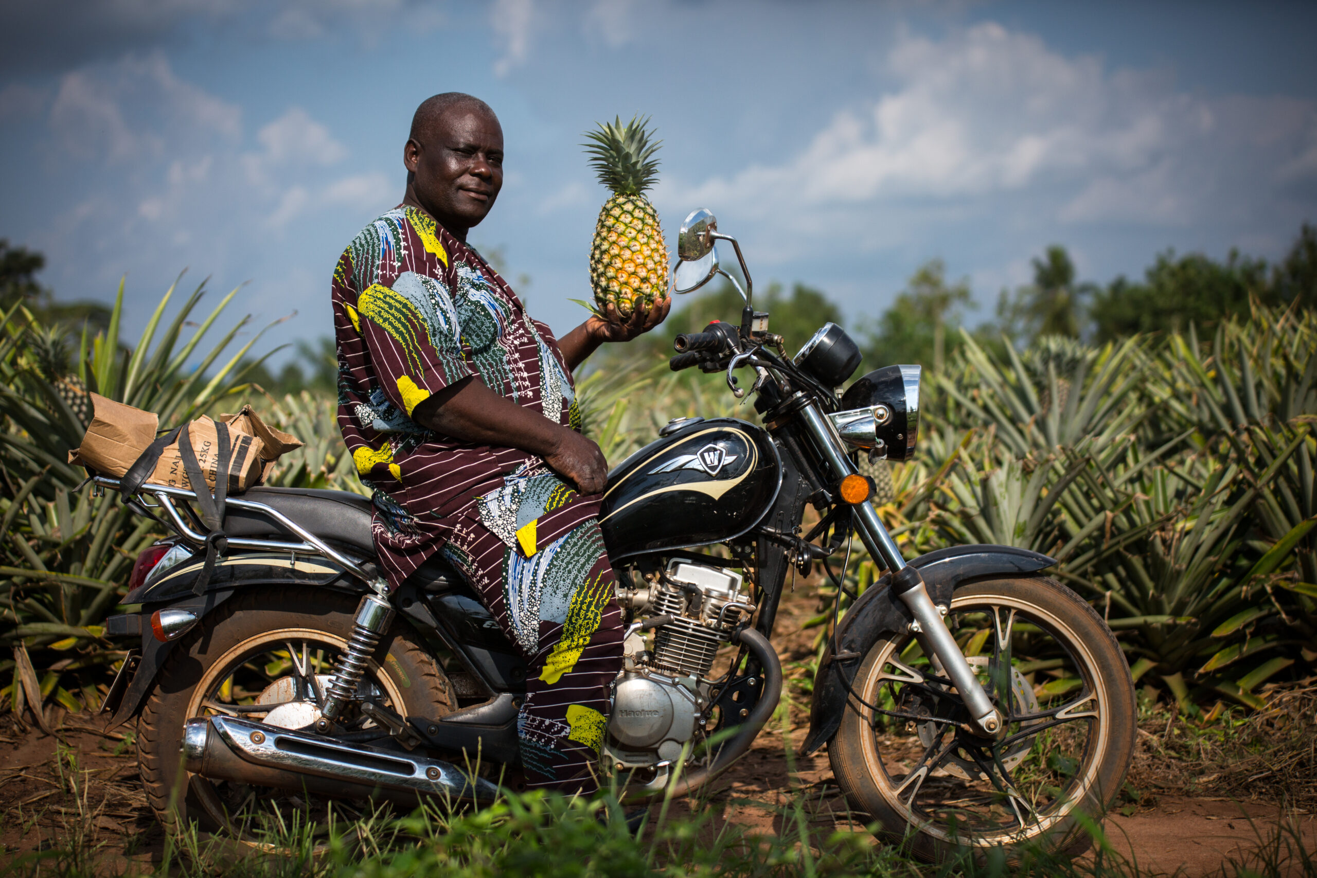 Man on a motorcycle holding a pineapple in a pineapple field in Benin.