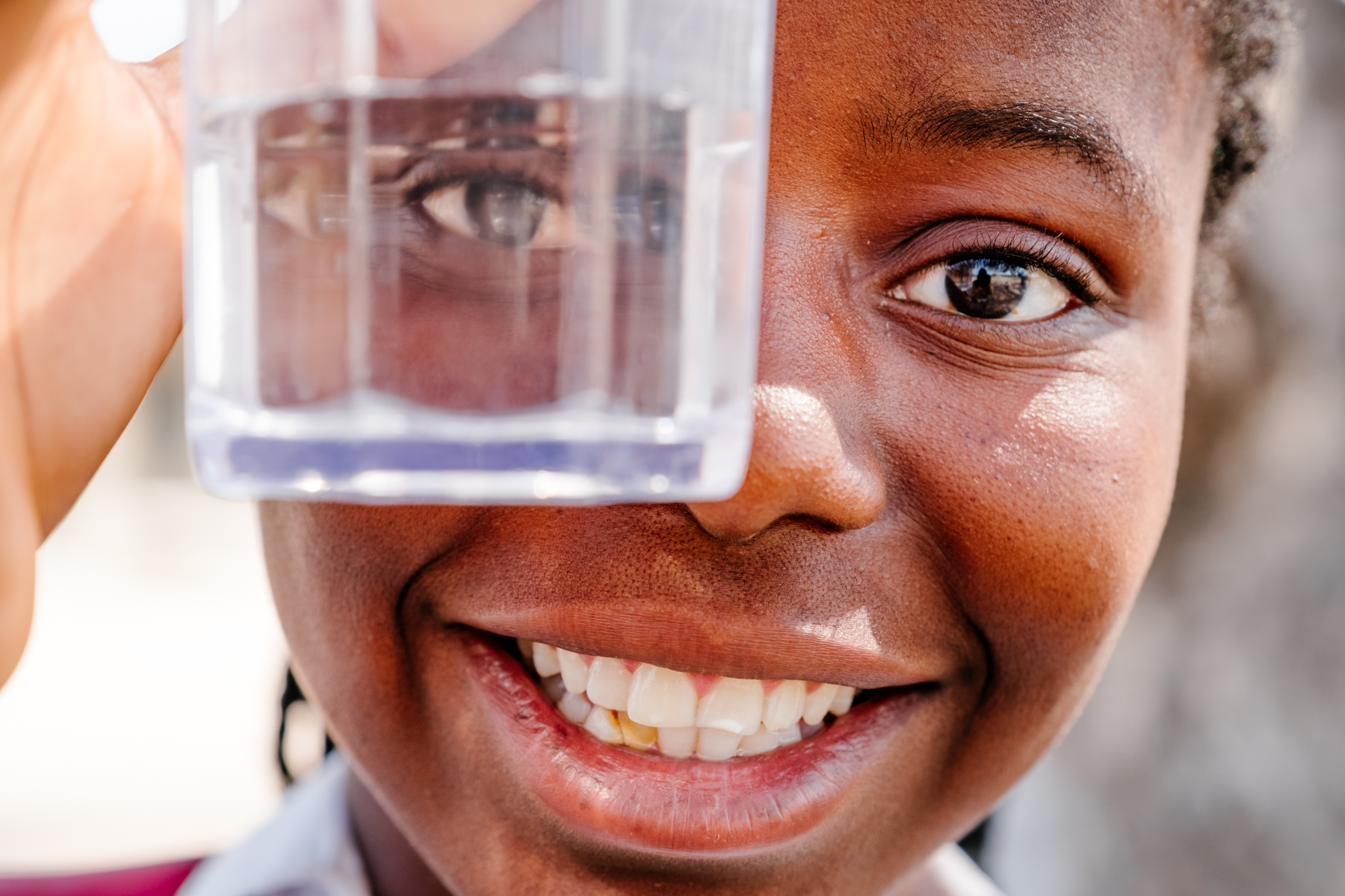 Girl in Mozambique looking through a glass for drinking water and smiling.