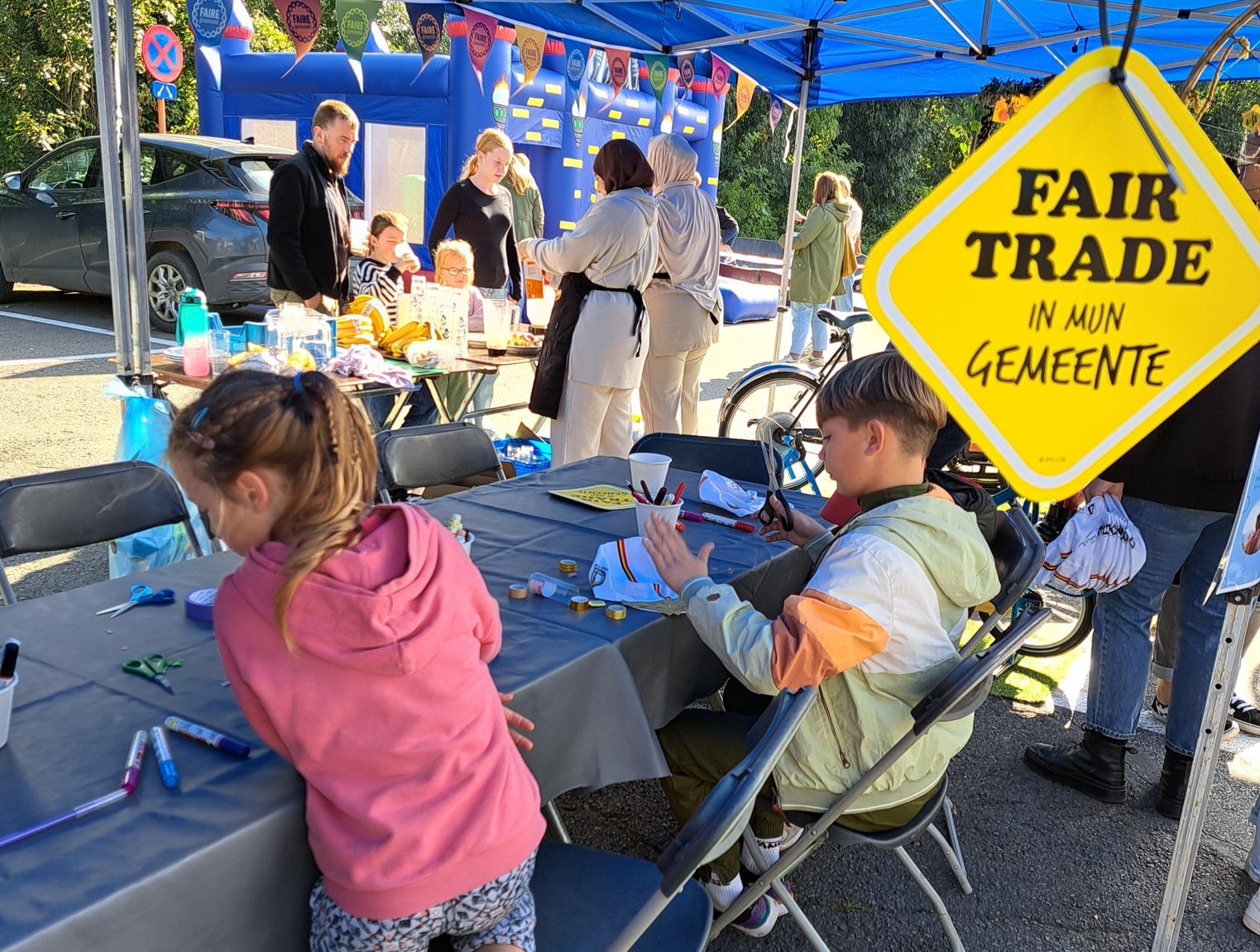 children sitting at a stand with fairtrade board in the foreground