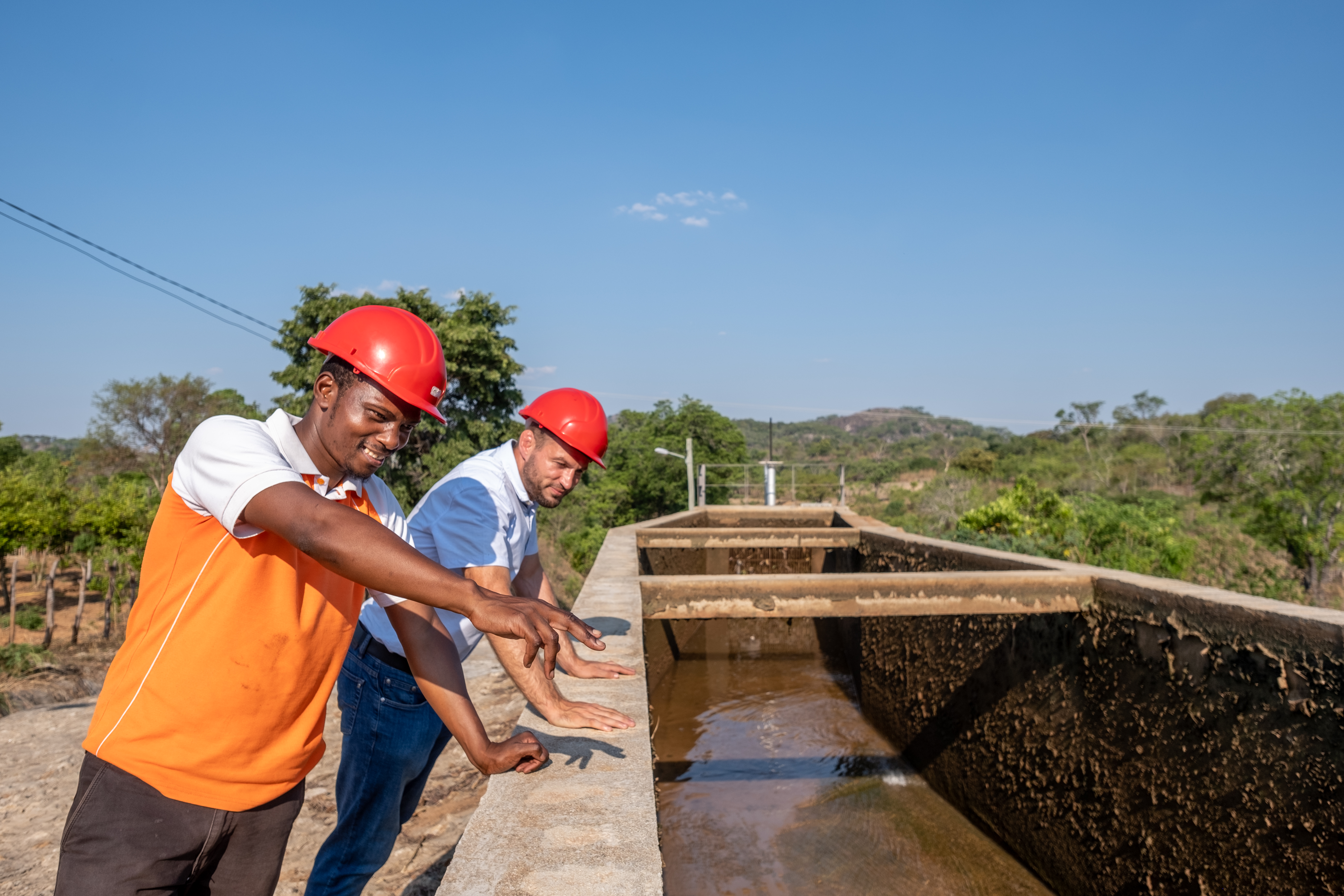 Two men wearing safety helmets look at a hydro-power plant.