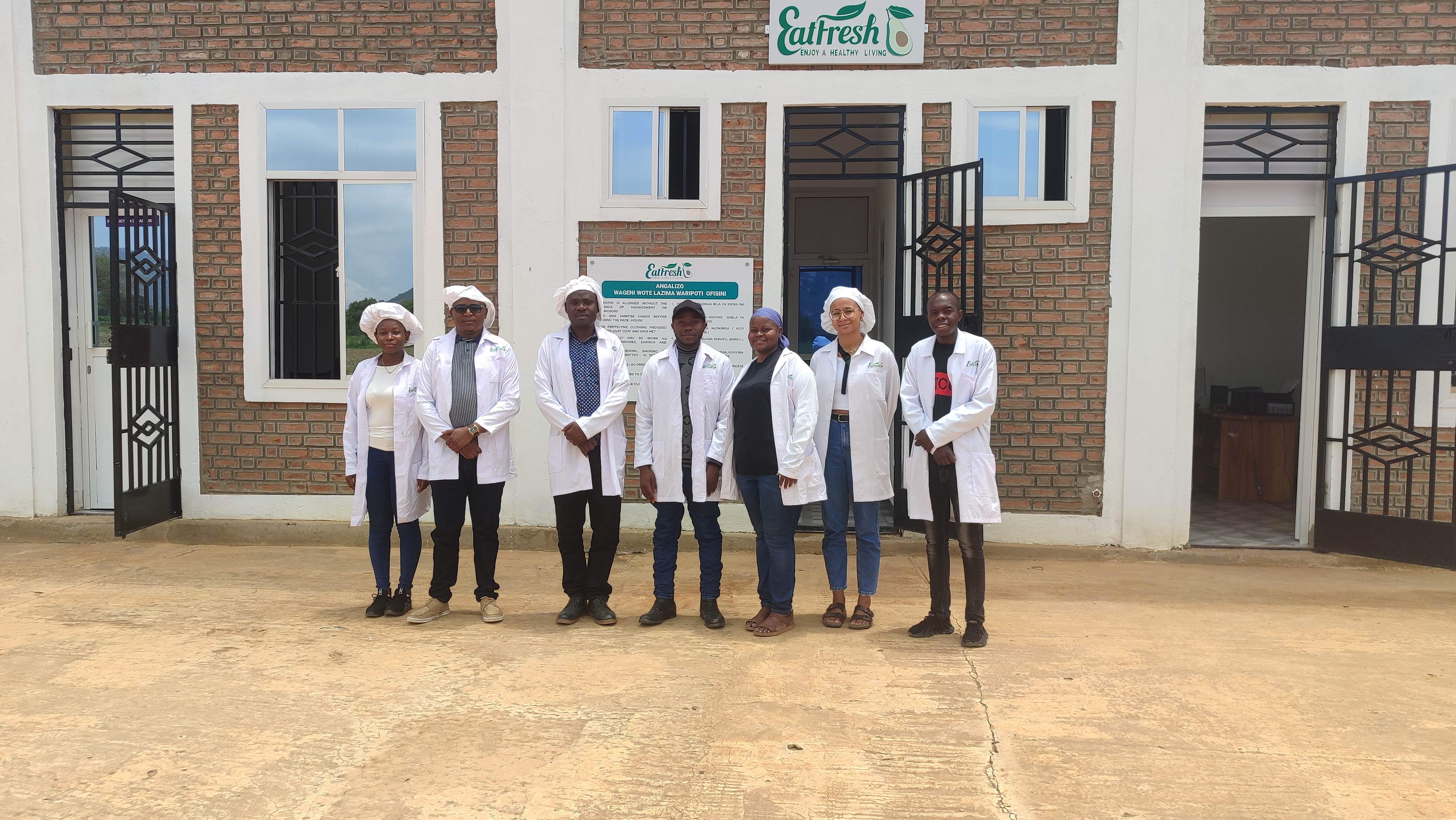 Group of people with white coats in front of a food prcessing company.
