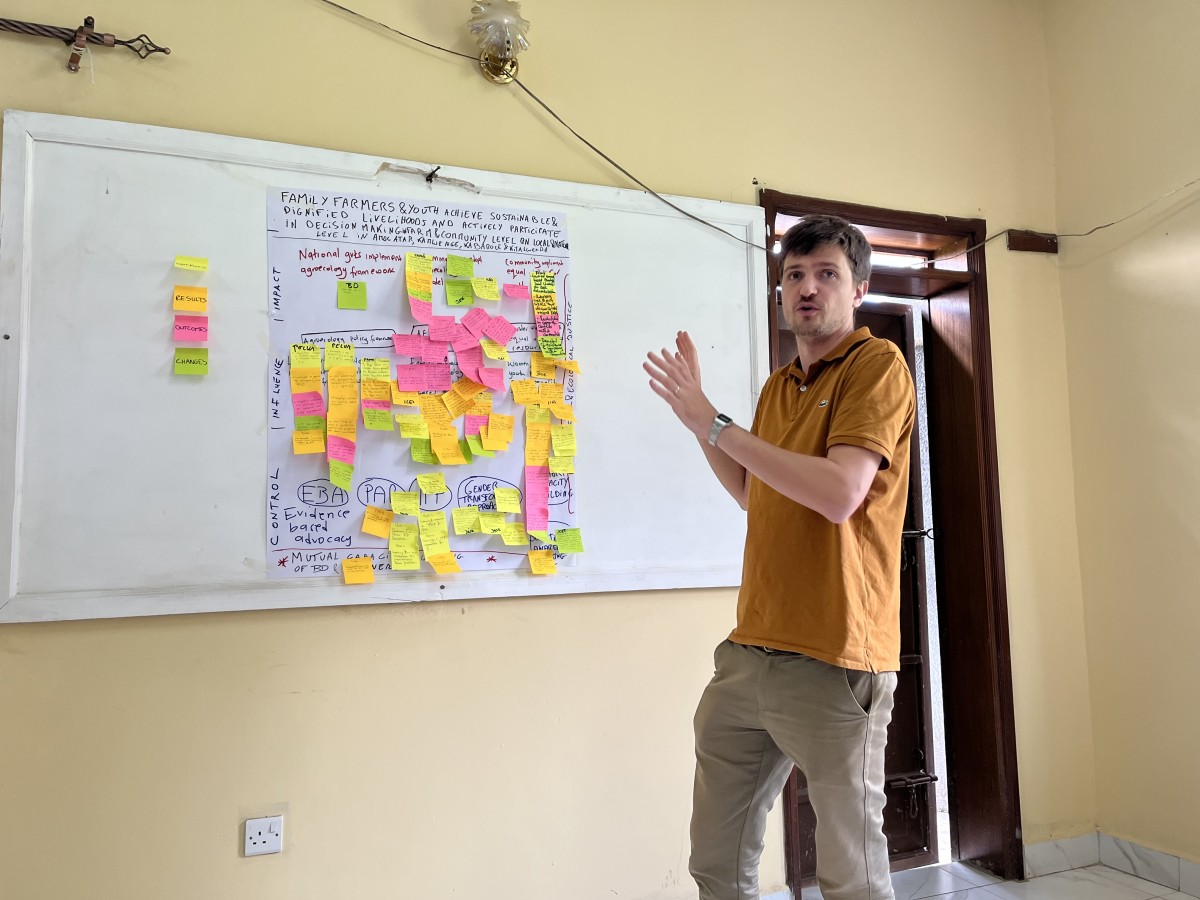 A man presenting in front of a white board with post its.