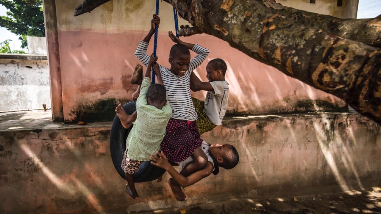 3 children playing, holding on to a swing connected to a tree.