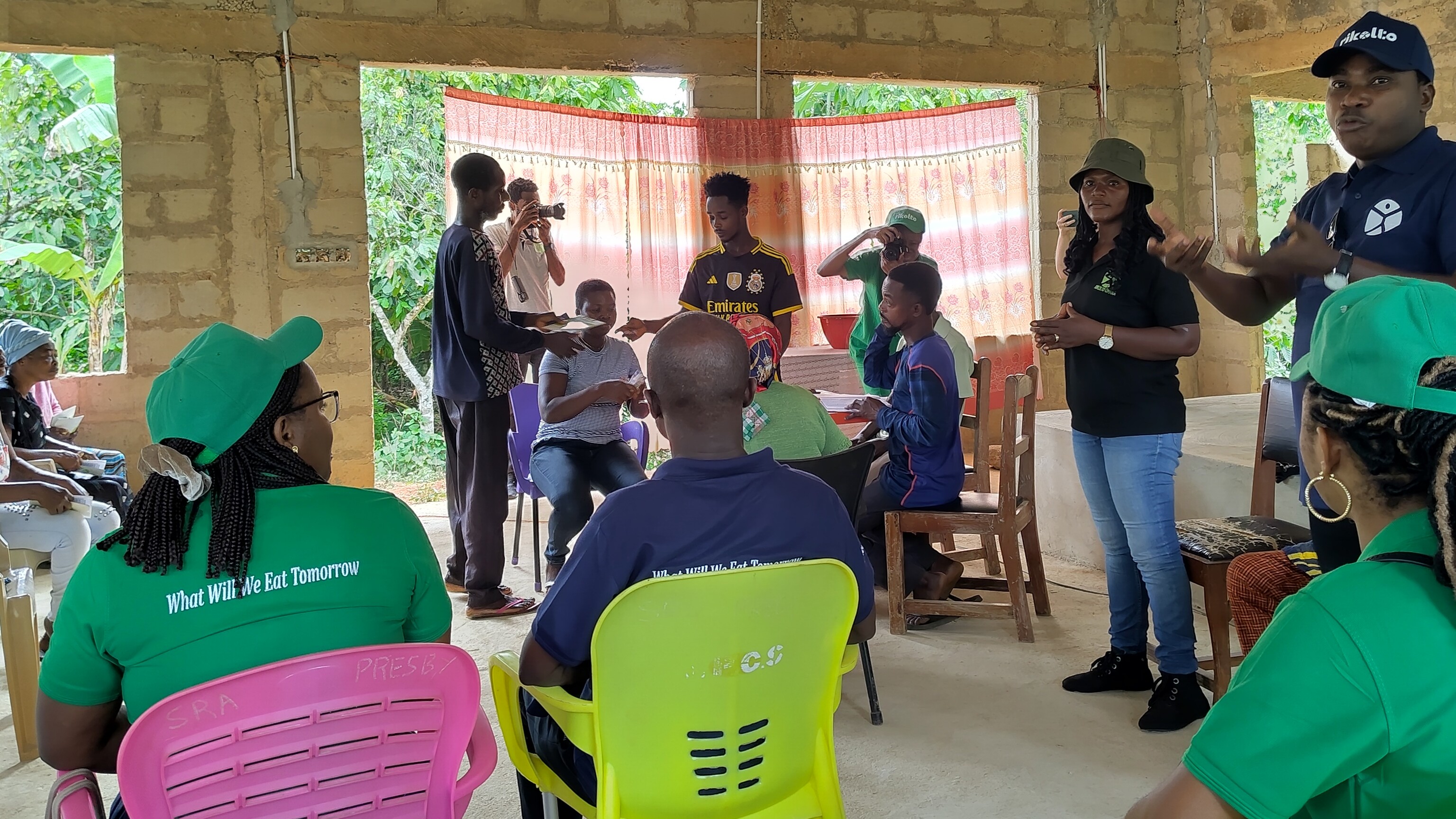 Group of people sitting in a building that's being constructed on plastic and wooden chairs.
