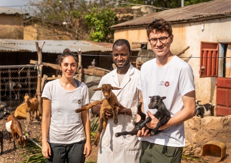 2 men and one woman posing for a picture with two little goats in their hands.