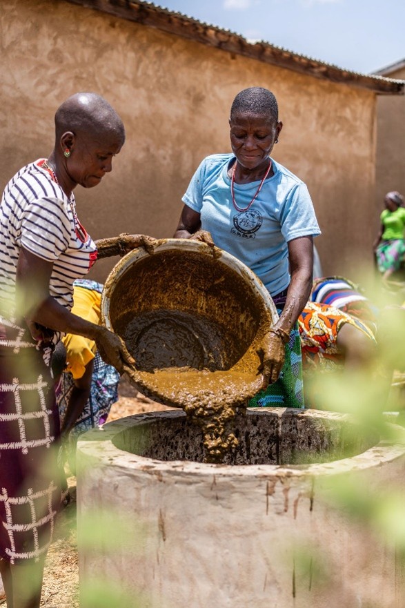 2 women adding organic waste to a biodigester.