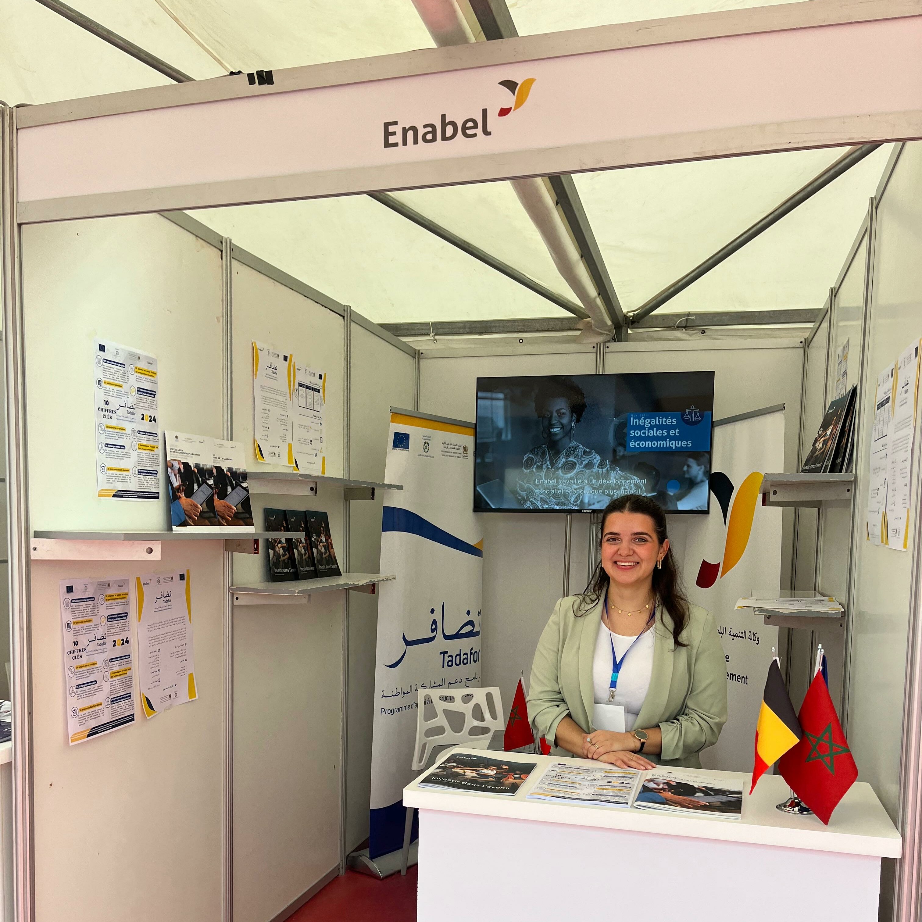 Young woman standing behind a desk at an Enabel stand during a forum.