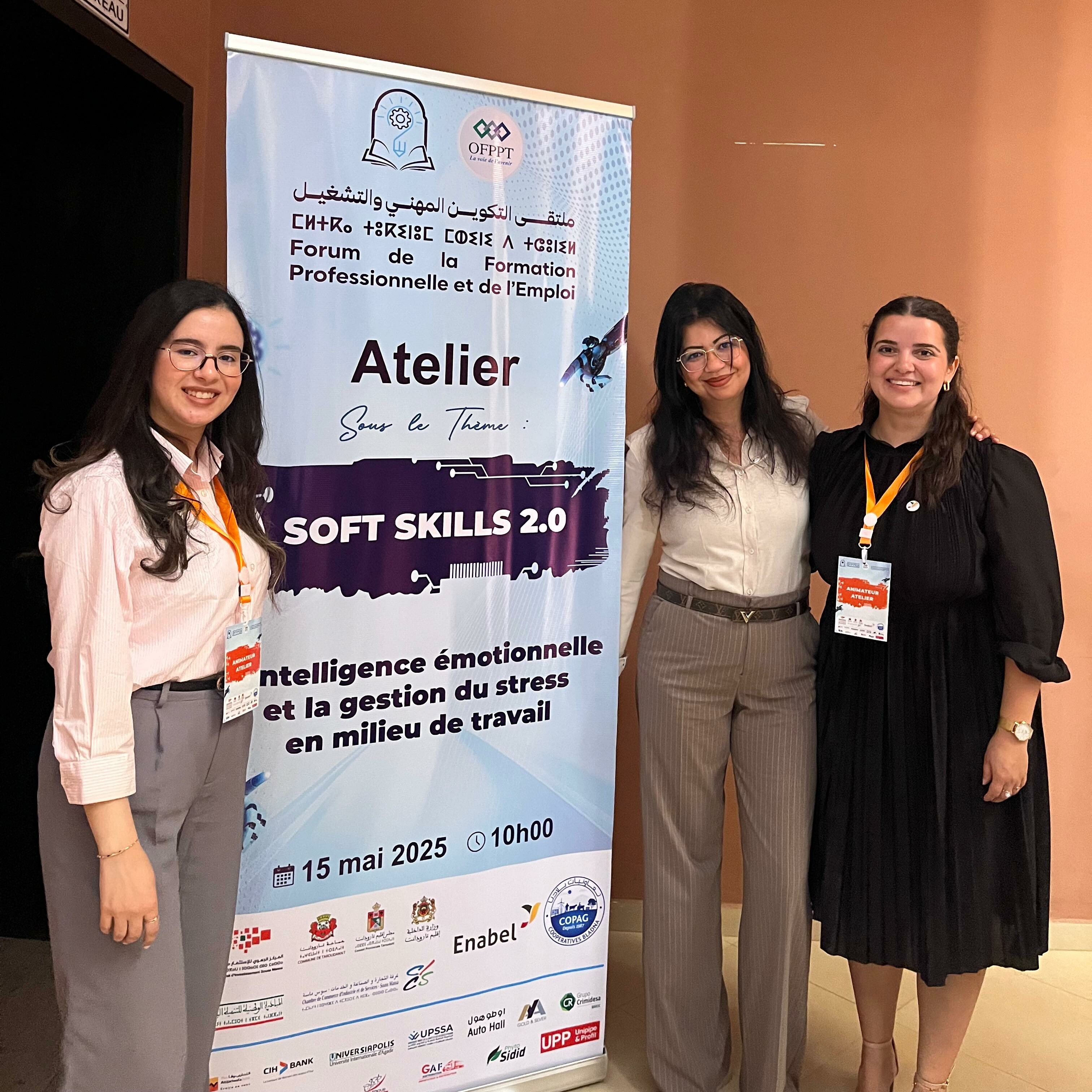 3 young women pose next to a banner of a soft skills workshop in Morocco