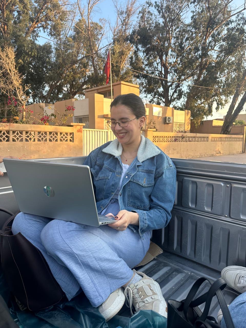 Young woman sitting on a bend with her laptop on her lap.